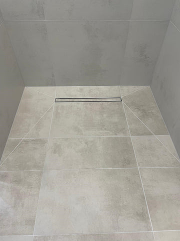 A tiled shower floor with a linear insert drain cover.