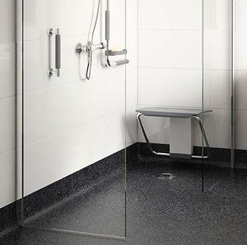 This image shows a modern, accessible shower with a foldable seat and handheld showerhead, designed for wheelchair users. The shower has a sleek glass door and a non-slip floor.
