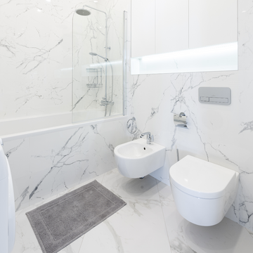 Modern small bathroom with white marble walls and floating fixtures.
