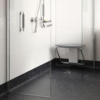 This image shows a modern, accessible shower with a foldable seat and handheld showerhead, designed for wheelchair users. The shower has a sleek glass door and a non-slip floor.