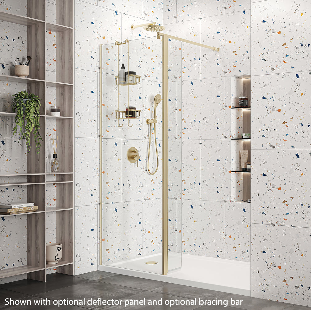 Roman Haven Wetroom Shower Screen Panel 1000mm in brushed brass finish. Installed in a stylish bathroom with terrazzo tiles and optional deflector panel.